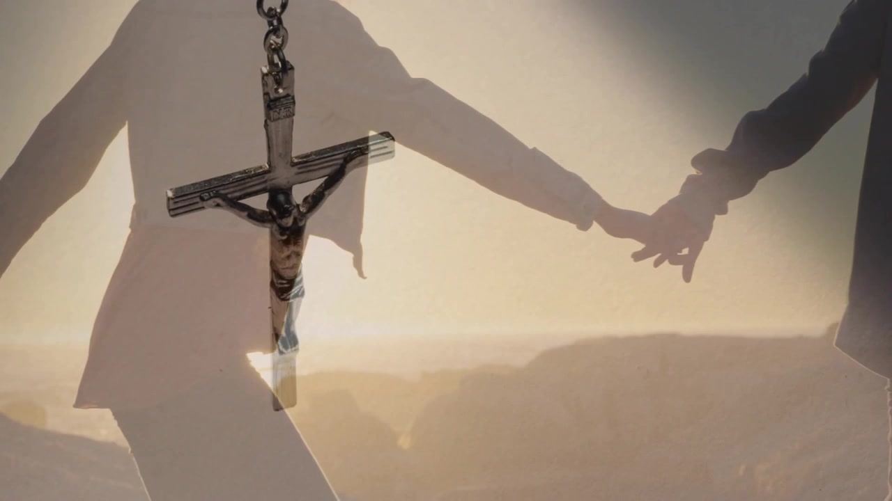 Clip publicitaire montrant un pendentif crucifix se balançant dans le cadre, le focus se déplaçant vers un couple marchant sur le rivage au coucher du soleil.