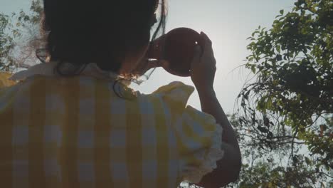 A-close-up-shot-of-an-Asian-female-eclipsing-the-morning-sun-as-she-joins-2-pieces-of-a-broken-clay-pot-together-covering-the-sun,-India