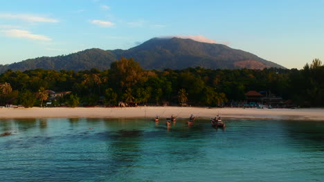 An-aerial-shot-from-the-ocean-side-facing-white-sand-beach,-resort,-green-trees-and-mountain