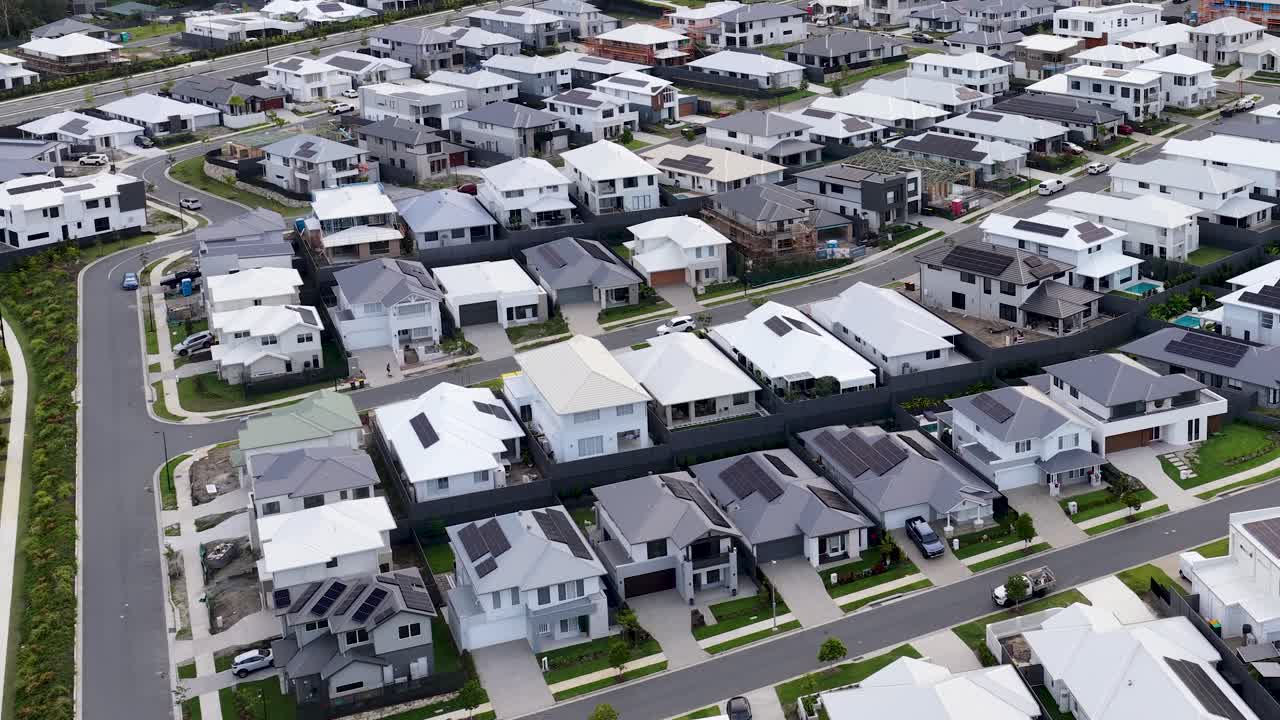 Drone glides above contemporary suburban neighborhood, revealing neat streets, modern houses, and overcast lighting