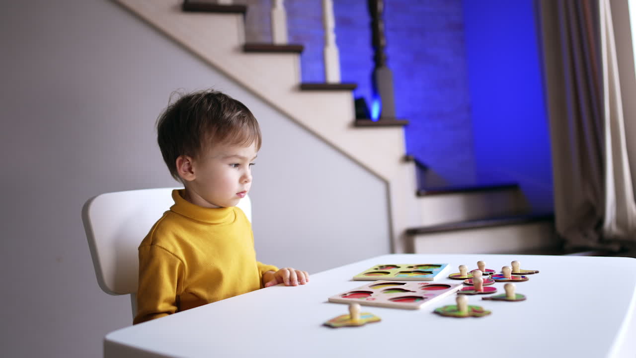 Calm focused toddler boy looks at pieces of puzzles. Cute kid distracts from puzzles and looks aside.