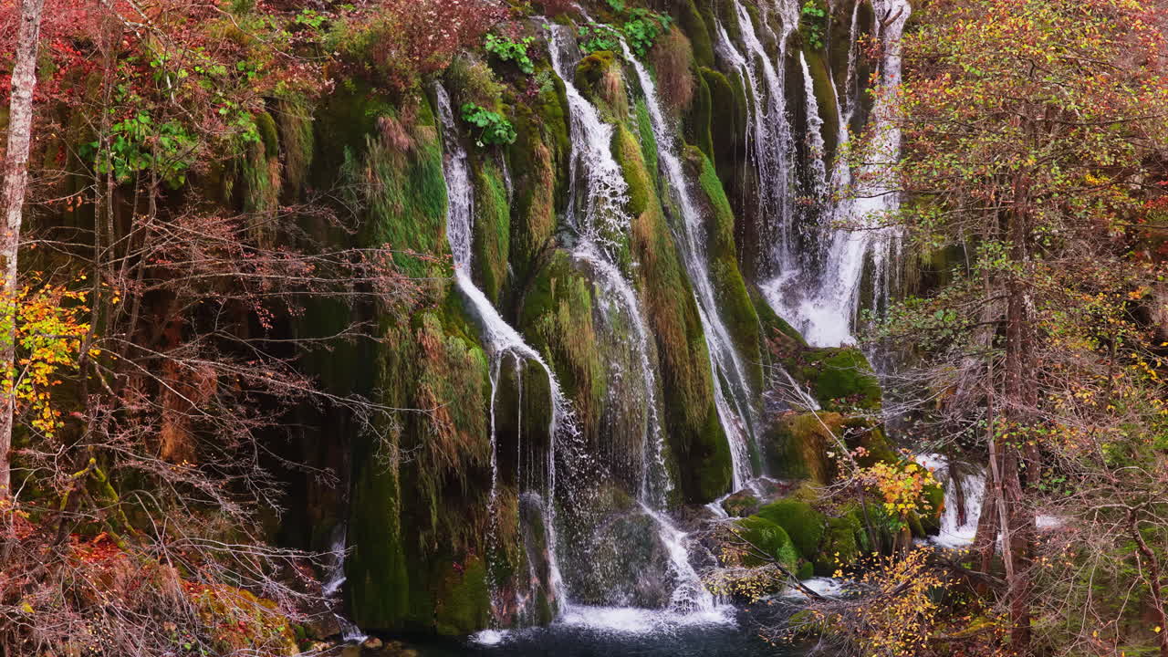 Vista aerea da drone di cascate a gradoni che scorrono su scogliere coperte di muschio e vegetazione lussureggiante nel Parco nazionale dei laghi di Plitvice, Croazia