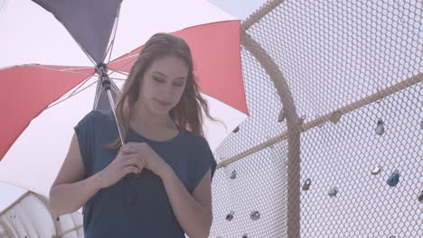 low angle shot of millennial female walking across a love lock bridge with an umbrella on a sunny day