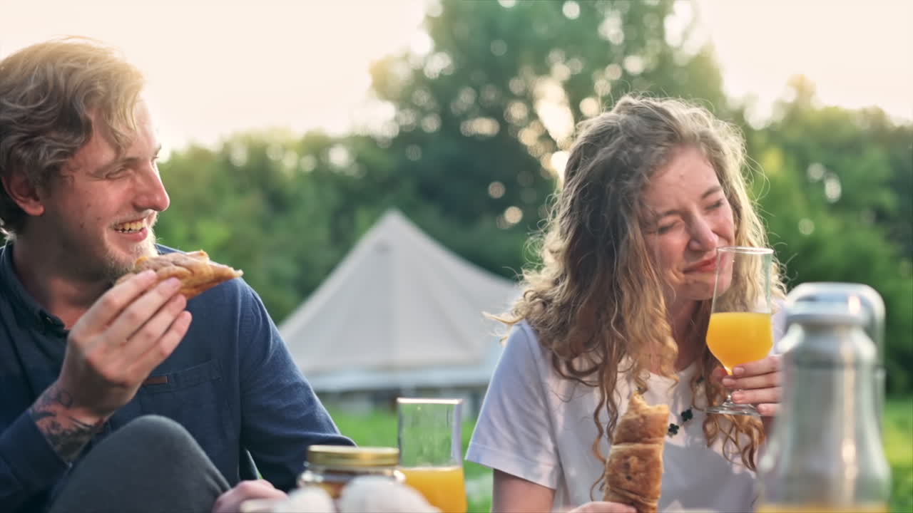 A couple having breakfast in the nature at glamping. Drinks, food, talking and smiling. Tent on the background. Slow motion