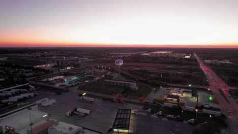 Vista-Aérea-Del-Crepúsculo-De-Monee,-Illinois:-Brillante-Puesta-De-Sol-Sobre-La-Expansión-Urbana,-Las-Carreteras-Y-La-Torre-De-Agua