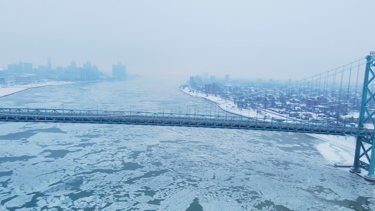 Drone video of Ambassador Bridge curves across snowy riverbanks with Detroit skyline in distance