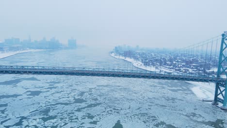 drone video of ambassador bridge curves across snowy riverbanks with detroit skyline in distance