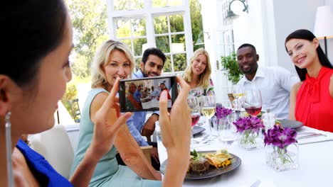 mujer fotografiando a amigos sentados a la mesa