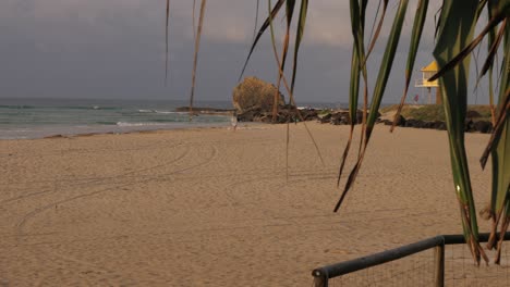 sandy shore of currumbin beach with ocean waves, lifeguard tower, and surfers on cloudy day in queensland, australia. wide shot