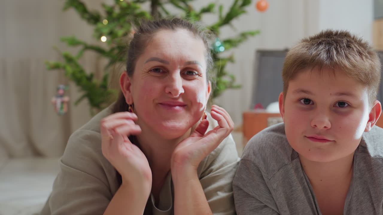 woman and son looking focused while lying on marble floor cozy home environment festive background featuring decorated christmas tree with lights warm family bonding moment