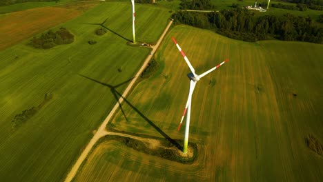 drone shot of a few wind turbines working and generating green electric energy on a green field on a sunny day, use of renewable resources of energy, top down shot