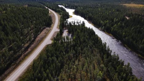 Vista-Aérea-Siguiendo-El-Río-Y-La-Carretera-En-Un-Gran-Bosque-De-Coníferas-En-Finlandia