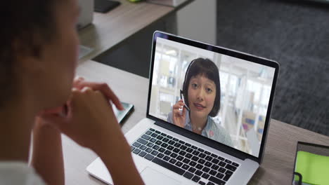 mujer de negocios afroamericana sentada en un escritorio usando una computadora portátil haciendo una videollamada con una colega