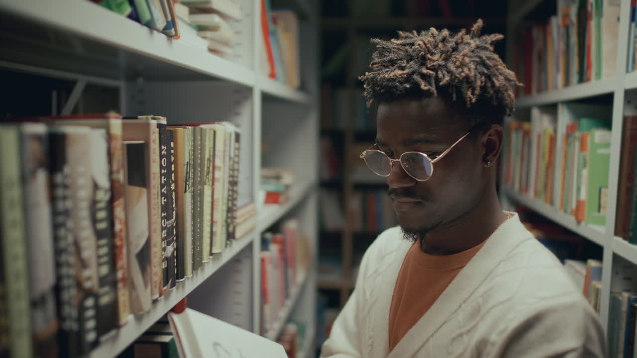 joven afroamericano leyendo un libro entre los estantes de la biblioteca