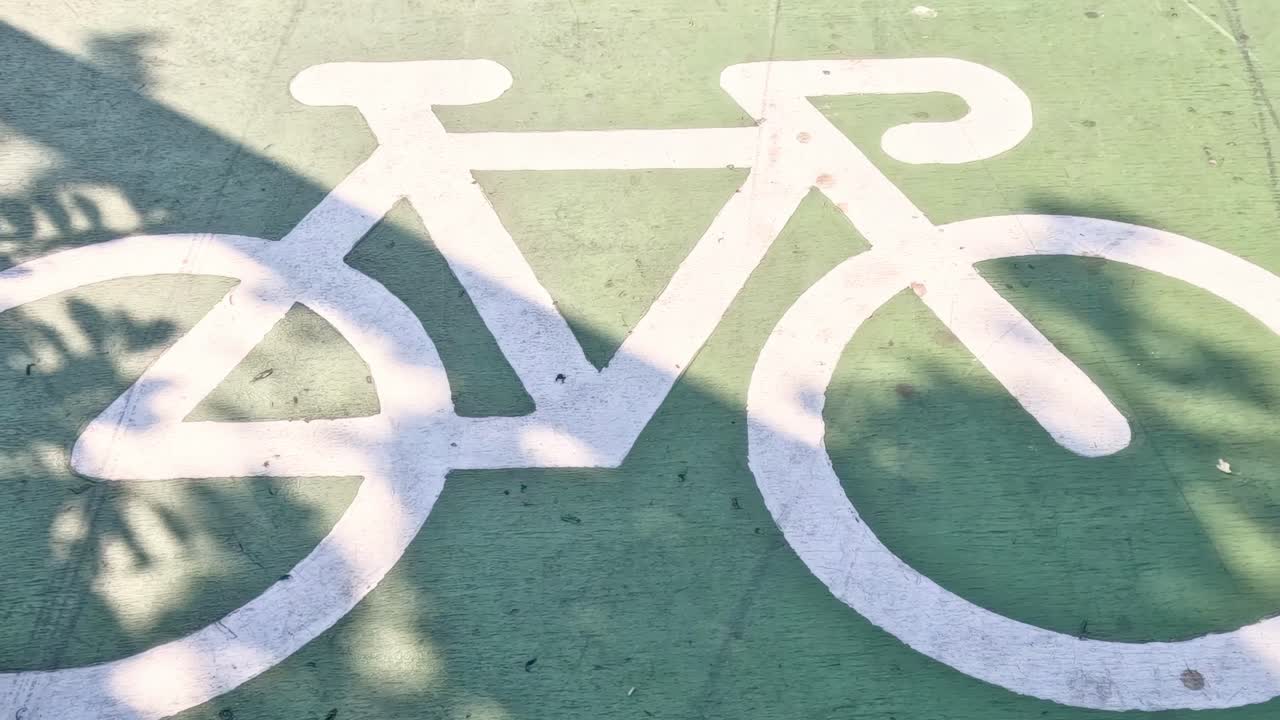 Tree shadows move across a white bicycle symbol on a green path, creating dynamic patterns.