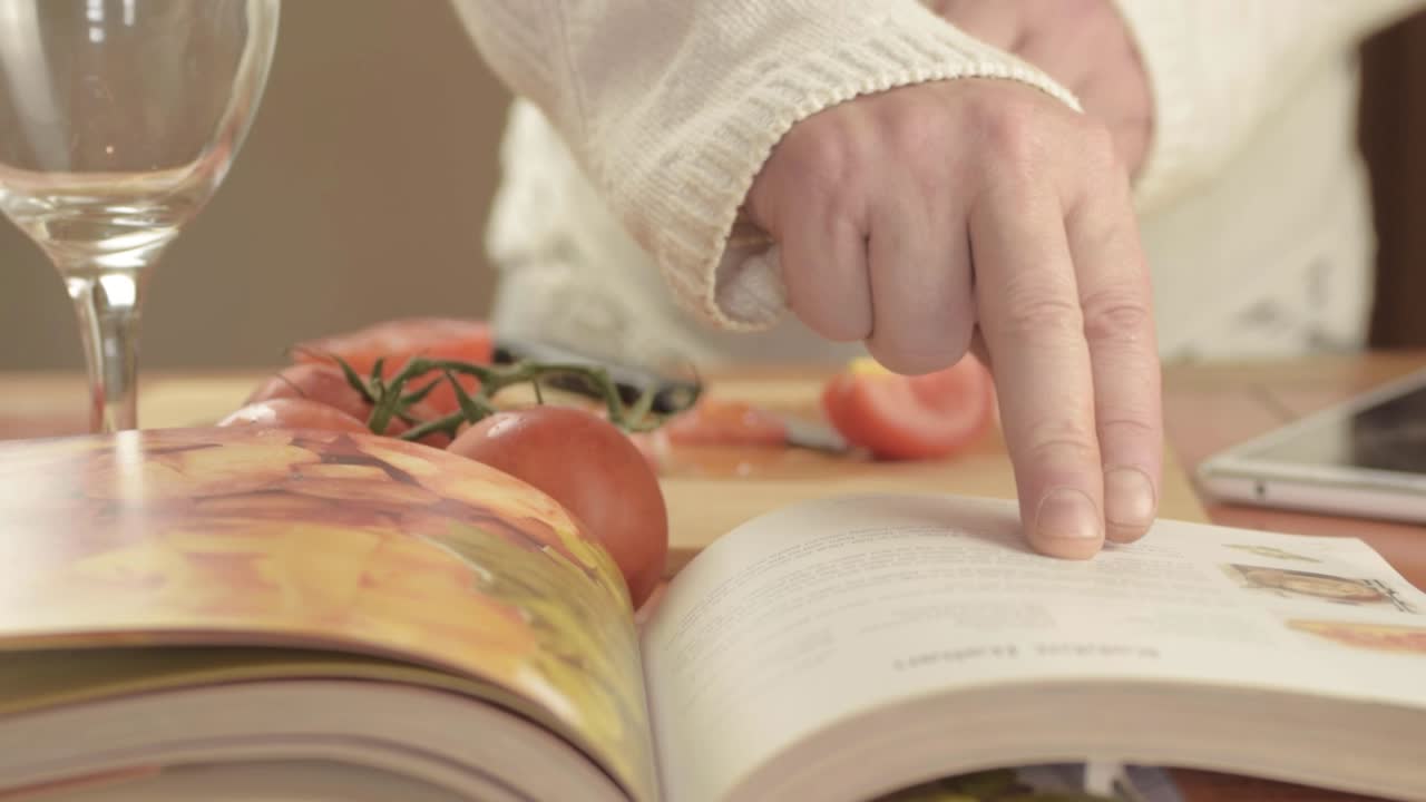 manos cortando tomates frescos de vid en la cocina con el libro de recetas de primer plano