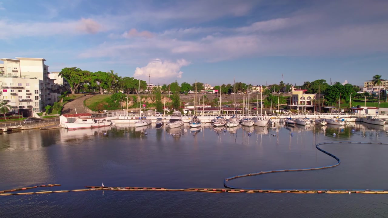 Ripresa aerea con drone ad alta angolazione che vola in avanti e panoramica a destra sopra il fiume Ozama verso yacht e barche ormeggiate a Marina Bartolome Colon a Santo Domingo