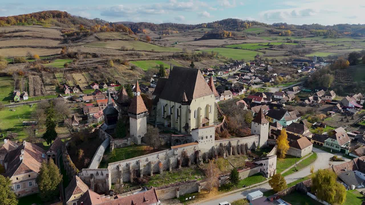 The camera pans forward, gradually revealing the impressive fortified medieval church and its surrounding village.