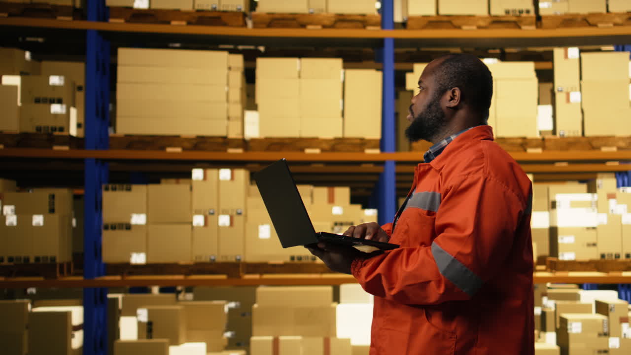 African american employee using laptop to handle logistics in industrial facility