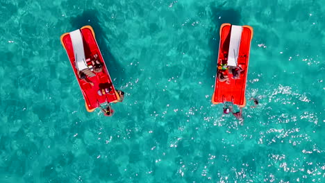 aerial shot of two red pedal boats with tourists in crystal clear blue waters of a sandy beach at a holiday resort