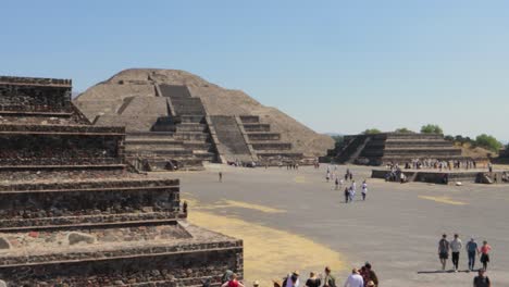 wide panning shot of the archaeological site of teotihuacan in mexico, with the pyramid of the moon and other ruins and people walking around on a clear and sunny day