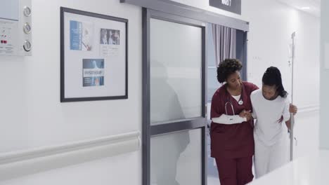 médica afroamericana ayudando a una paciente caminando por el pasillo del hospital, cámara lenta