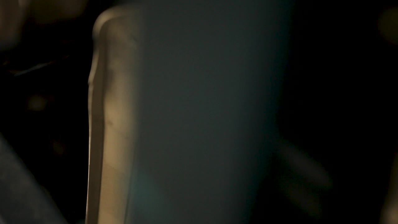 vista angular de primer plano, cámara de mano captura un complejo objeto metálico, rico en líneas curvas y rectas, agujeros y ranuras, dramáticamente iluminado desde la esquina superior izquierda contra un fondo negro