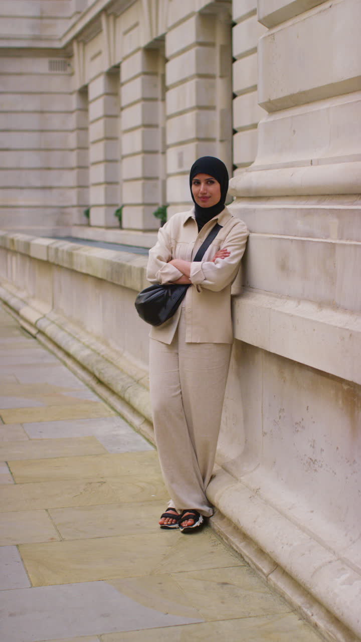 Vertical Video Portrait Of Smiling Muslim Businesswoman Wearing Hijab And Modern Business Suit Standing And Folding Arms Outside City Office Buildings 2