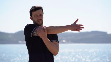 handsome young sportsman stretching arms at riverside