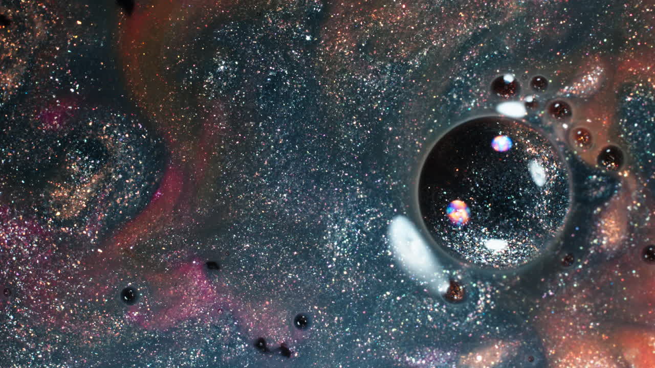 Colorful liquids and oil droplets mix in an abstract, sparkling macro shot with cosmic tones