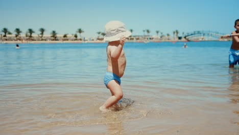 Dulce-Niño-Dando-Sus-Primeros-Pasos-En-El-Agua-De-Mar.-Lindo-Niño-Salpicando-Agua