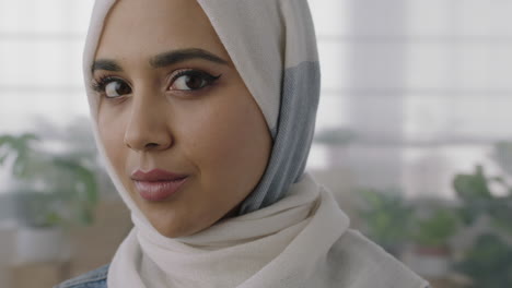 close up portrait of young muslim business woman turns head looking at camera smiling confident wearing traditional hajib headscarf in office workspace background