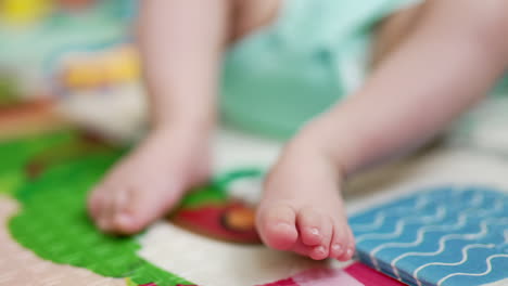 Tiny feet of a baby lying on the bed on his back. Child lies calmly on a colorful cover. Close up. Blue backdrop.