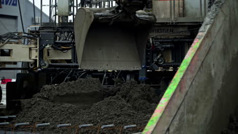 excavator bucket dumping aggregate material in a concrete paving machine