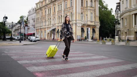 woman with luggage walking across a crosswalk in a city street