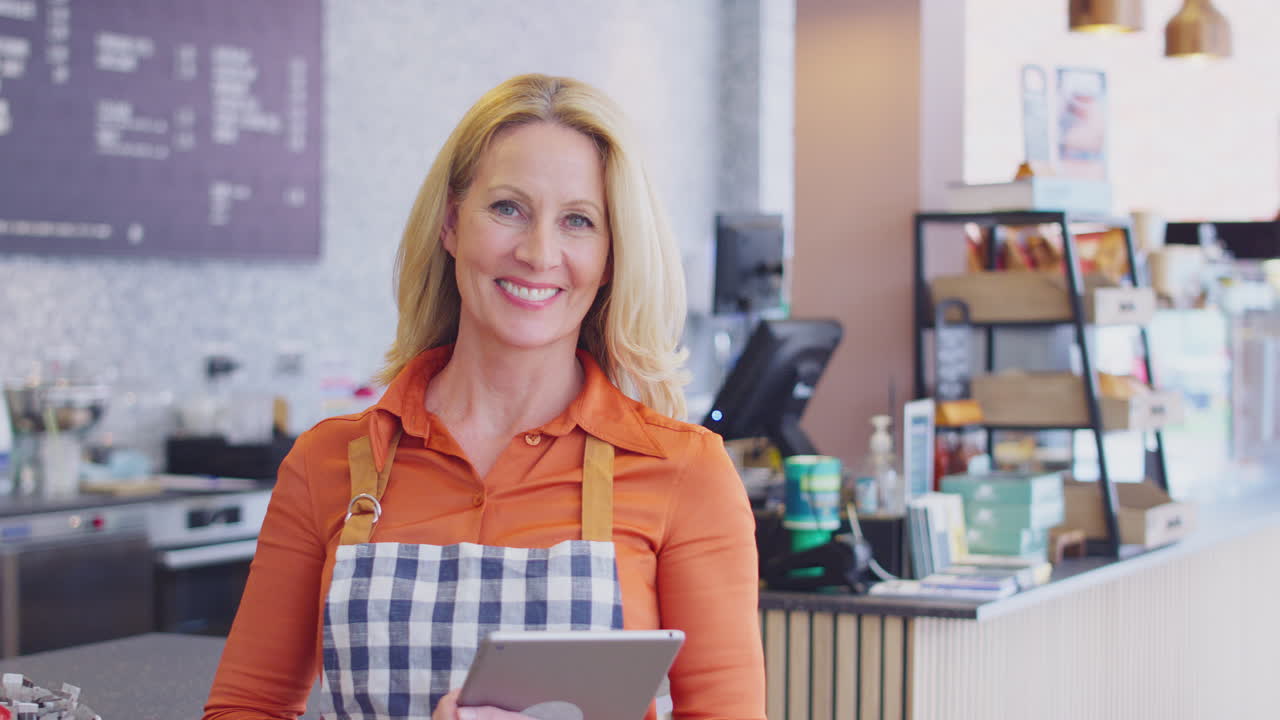 Portret van volwassen vrouwelijke eigenaar van een koffiezaak of restaurant die een digitale tablet gebruikt.