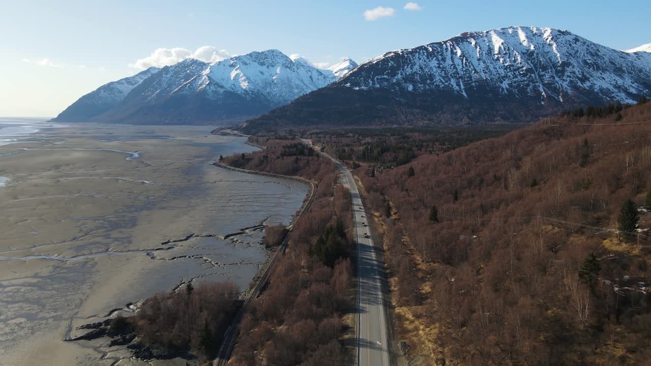 Drone 4K che vola lungo la costa dell'Alaska mostrando alberi, neve e montagne la sera, all'inizio della primavera