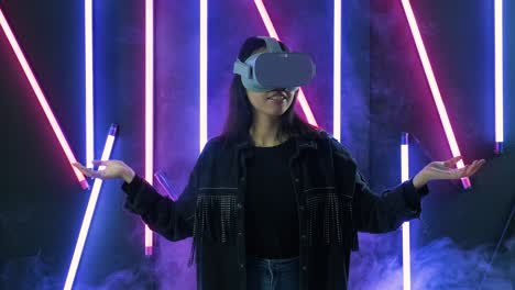 young woman looks around and wonders how amazing  in the vr headset. virtual reality helmet on color lighting smoke background