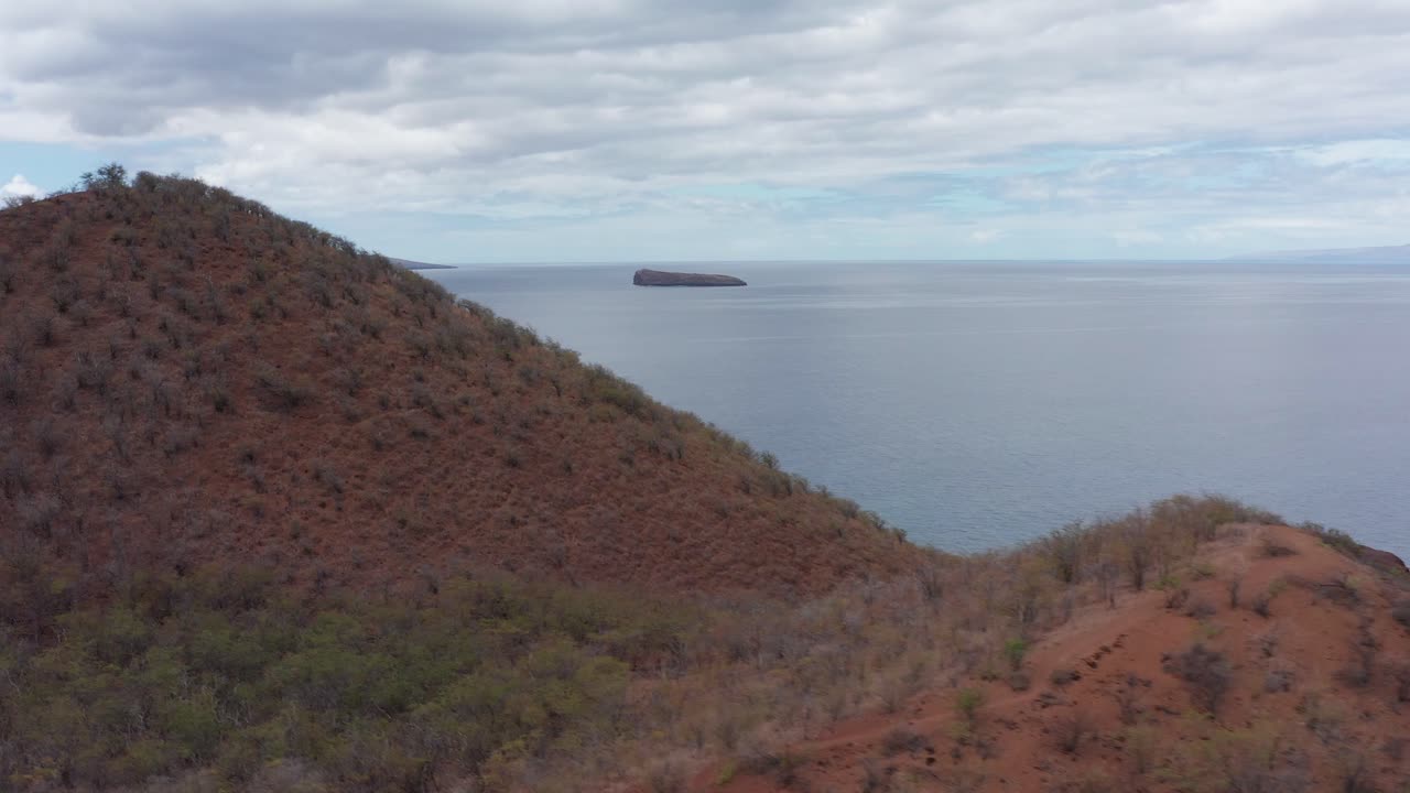 Close-up aerial shot flying over the cinder cone crater Pu'u Olai towards Molokini Crater and the Hawaiian island of Kaho'olawe off the coast of South Maui, Hawai'i