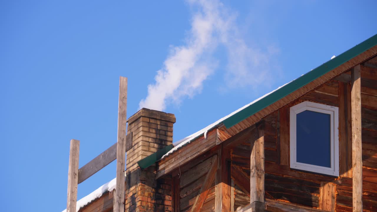 humo de una chimenea de ladrillo en un techo de casa de madera en invierno contra un cielo azul