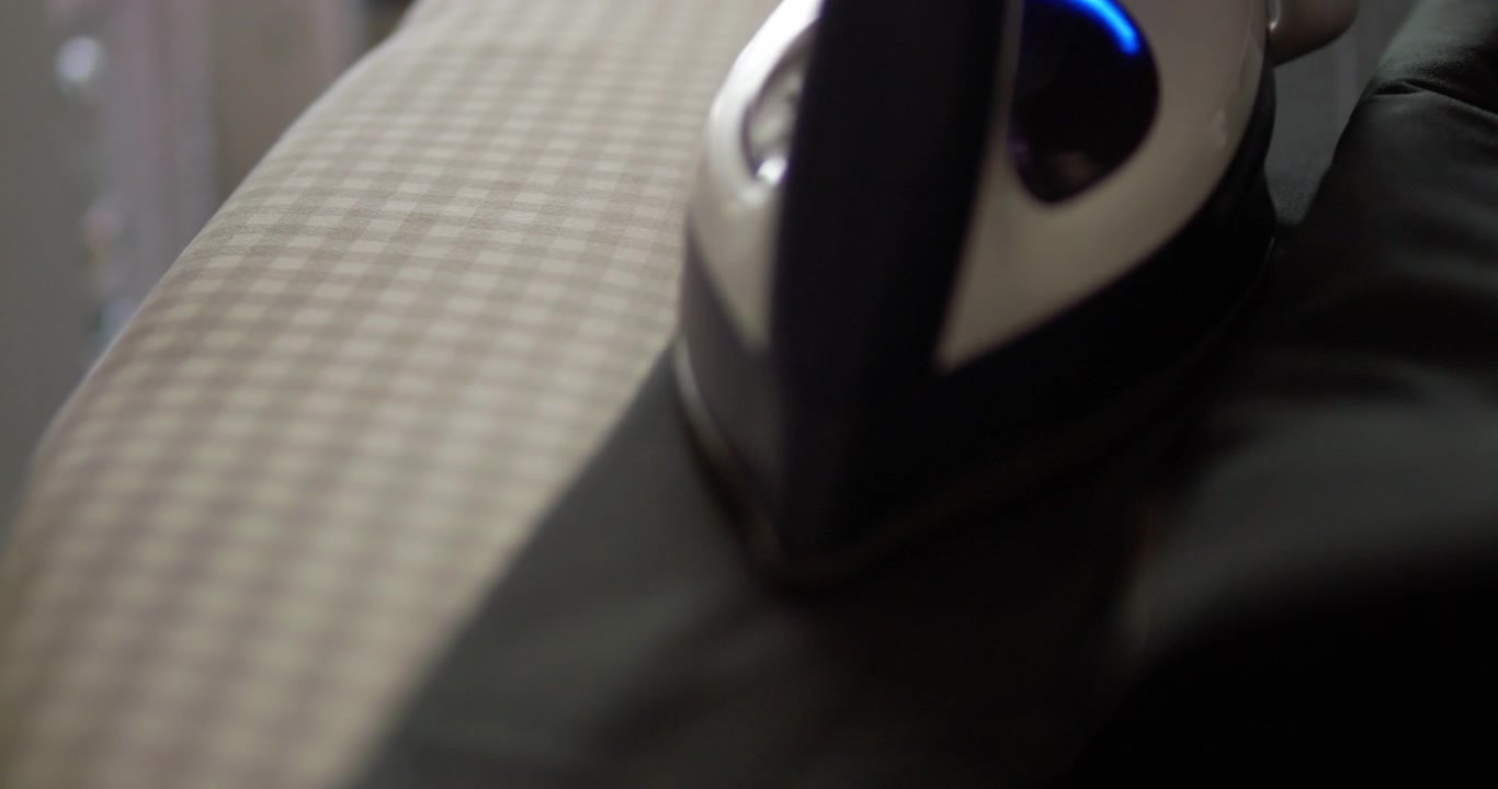 Slow motion close-up shot of an individual pressing a pair of pants using an electric iron and an ironing board.