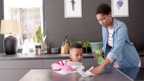 african american mother and son cleaning countertop in kitchen, slow motion