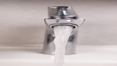 close up of water flowing from a chrome faucet