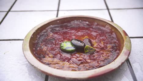 close-up pan of slow-motion rain flooding a red flower clay jar with stacked pebbles