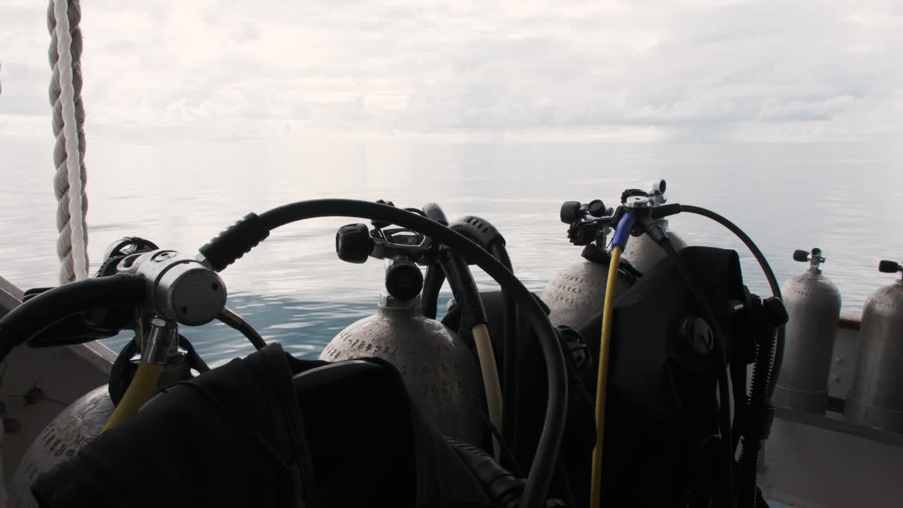 Scuba tanks stand ready on a boat deck, the vast ocean and a cloudy sky stretching out in the background