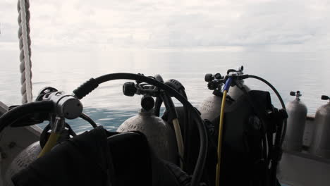 scuba tanks stand ready on a boat deck, the vast ocean and a cloudy sky stretching out in the background