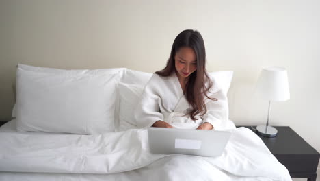 성공적인 아시아 여성이 호텔 침대에서 노트북을 사용하여 온라인 채팅 및 인터넷 작업