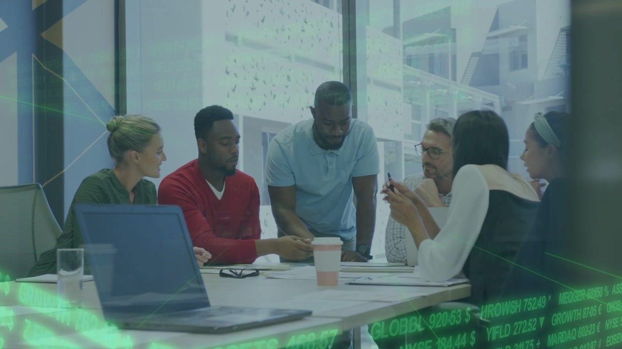 Standing male leaning and pointing at docs business team reading data with green ticker over laptop