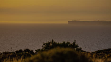 Hazy-golden-sunset-overlooking-the-Mediterranean-Sea-and-distant-cliffs---time-lapse