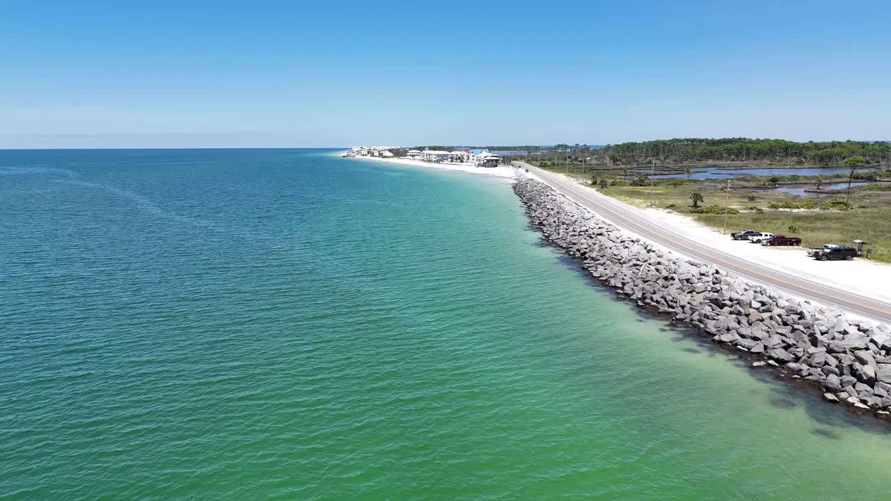 Dynamic drone fly near the curved coastal main road with stone breakwater beside turquoise seawater, Cape San Blas, Gulf County, Florida, USA
